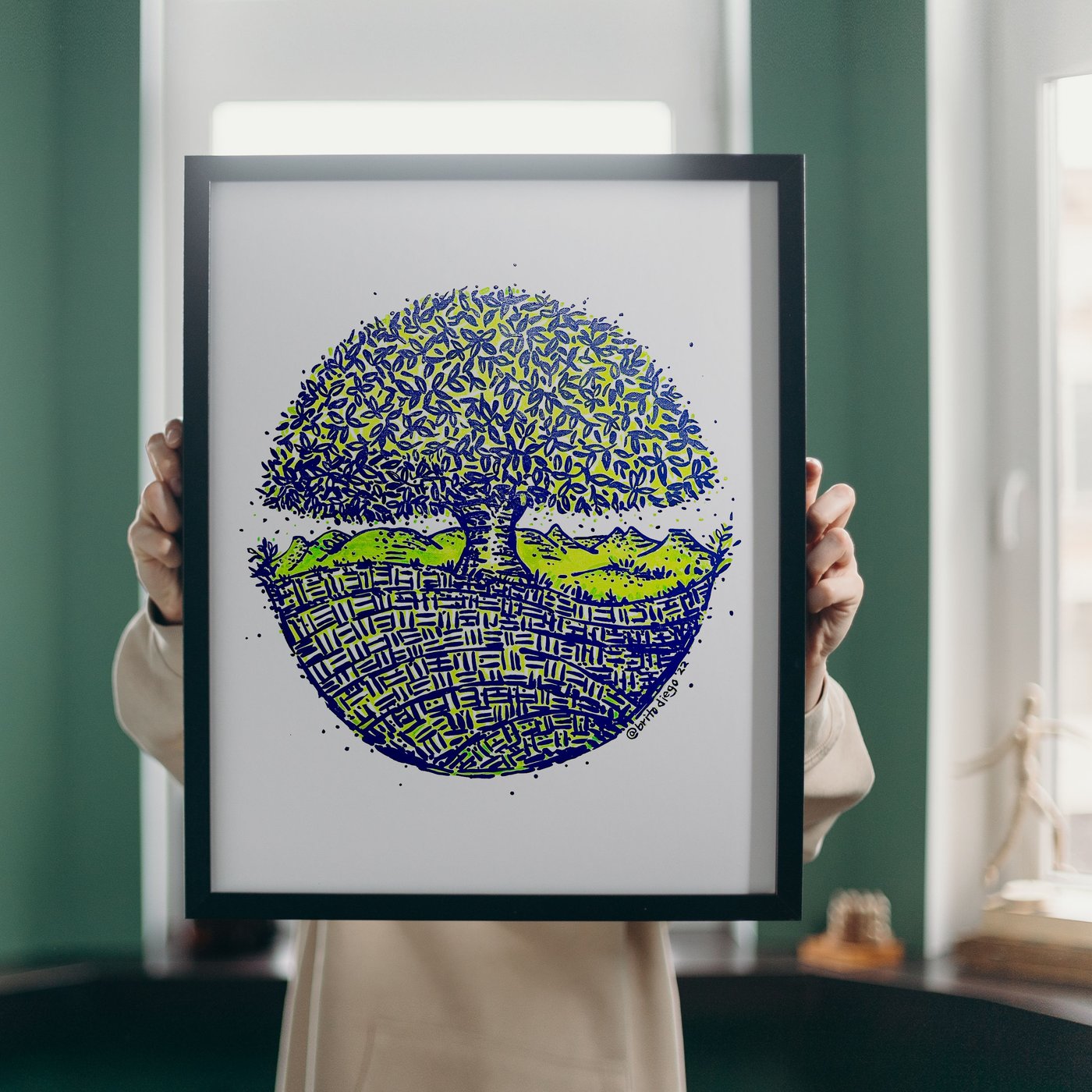 A framed Love Yourself Tree held in two hands — navy and lime on white, by Diego Brito